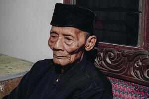 Thoughtful senior Asian man sitting on home sofa, looking away with thoughts, thinking over future retirement, planning, dreaming photo