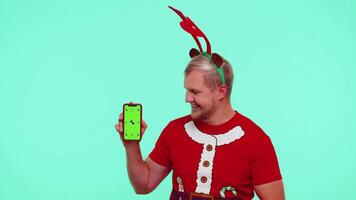 Man in t-shirt Santa Christmas and deer antlers showing mobile phone with green screen chroma key video