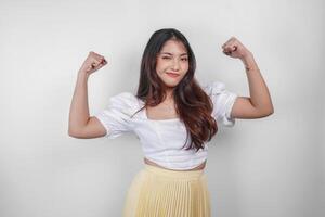 un retrato de asiático mujer demostración fuerte gesto por levantamiento su brazos y músculos sonriente con orgullo foto