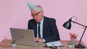 Sad upset lonely senior businessman celebrating birthday party alone, holds cake at pink office video
