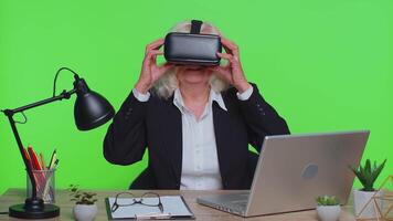 Senior businesswoman using headset helmet app to play simulation game watching virtual reality video