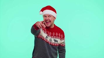 Man in red Christmas sweater smiling excitedly, pointing to camera, beauty choosing lucky winner video