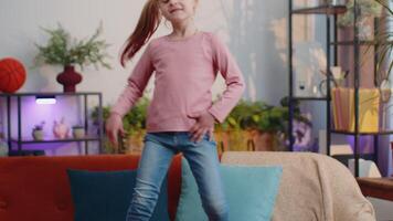 Happy child girl kid in headphones dancing and jumping while listening to the music at home alone video