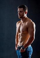 Athletic body. Half turned model guy is posing to the camera in the dark grey background. Full size photo. Strong muscular man. Closeup. photo