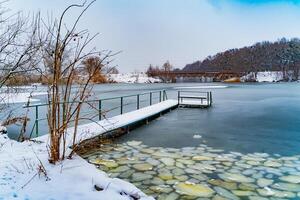 hermosa paisaje con congelado río y puentes terminado eso en invierno. imagen de naturaleza con nieve y el río cubierto con hielo cerca el bosque. foto