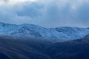 majestuoso nevadas montañas debajo un temperamental azul cielo, con laminación colinas en el primer plano en Escocia. foto