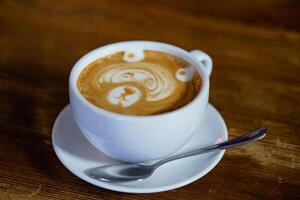 a white cup with latte and teaspoon stand on the platter on the table in the cafe. photo