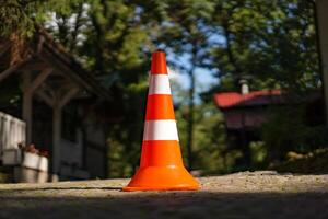 Orange street cone is on the ground with blurred background. Two stripes of white and orange traffic cone was put in nature near the houses in summer. photo