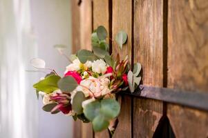 Bunch of fresh flowers with green leaves on the wooden door outside. Beautiful bouquet of tendy flowers decorated for wedding. photo