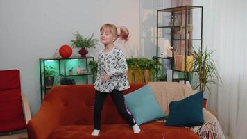 Happy child girl kid wears earphones dancing and jumping while listening to the music at home alone video