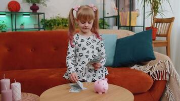Little toddler kid girl counting money dollar banknotes for future needs at home desk with piggybank video