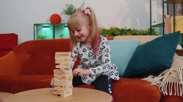 Funny happy one teenage kid girl play wooden tower blocks bricks game at home in modern living room video