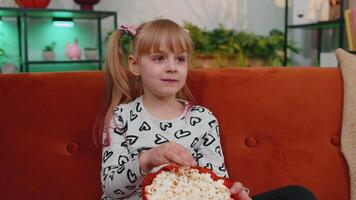 rolig liten barn flicka tittar på komedi video filma på tv, äter popcorn på bekväm soffa på Hem