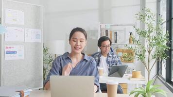skön ung kvinna asiatisk arbetstagare är Lycklig arbetssätt med bärbar dator, skriver, leende på skrivbord, tänkande av idéer, och koncentrering kreativ marknadsföring jobb i vit tillfällig kontor och börja sme företag. video