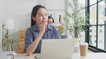 Beautiful young female Asian worker is happy working with laptop, typing, smiling at desk, thinking of ideas, and concentrating creative marketing jobs in white casual office and startup SME business. video