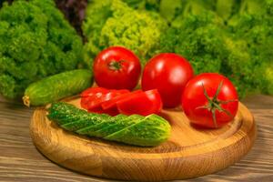 Fresh vegetables. Tomatoes and cucumbers on a wooden table. Green salad in the background. photo