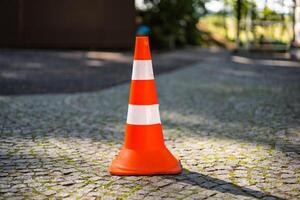 rojo naranja cono con un blanco raya en el pavimentación Roca la carretera. conducir la seguridad y construcciones concepto. de cerca. borroso antecedentes. foto