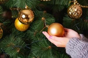 woman in knitted clothes holds a big orange ball in her hands on the background of the Christmas tree photo