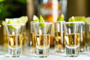 Glasses of silver and gold tequila with lime and salt on the table. Alcohol in short glasses, lime and salt, toned image. Close-up photo