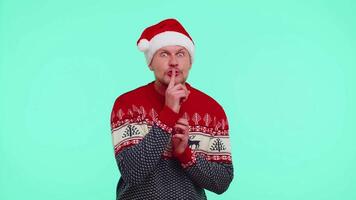 Man wears red Christmas sweater presses index finger to lips makes silence gesture sign, secret video