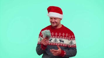 riches homme gagnant dans Noël rouge chandail et chapeau montrant gaspillage, lancement argent autour, achats video