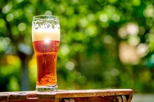 Beer in glass on wooden table with blurred city park on background, natural background. Closeup. photo