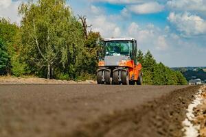 a steamroller with four wheels rides through the fresh asphalt to level the surface. Close-up photo