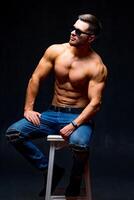 Sexual muscular man posing over dark background. Muscular body and strong abs. Looking at side. Studio shot. photo