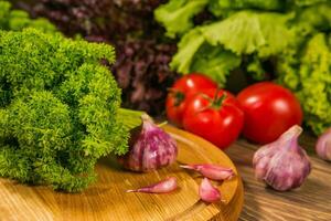 Juicy tomato and garlic on a wooden table. Green salad in the background. Healthy food,dieting consept. photo