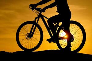 silueta joven hombre de ciclismo en puesta de sol antecedentes. bicicleta y ecología estilo de vida concepto foto