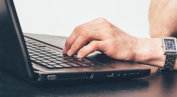 mano de un hombre con un reloj de pulsera mecanografía texto en el teclado a trabajo en el oficina foto