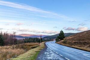 Scenic countryside road with lush greenery and a clear blue sky at dawn in Scotland. photo