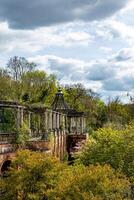 Ruined classical architecture with columns amidst lush greenery under a cloudy sky. photo