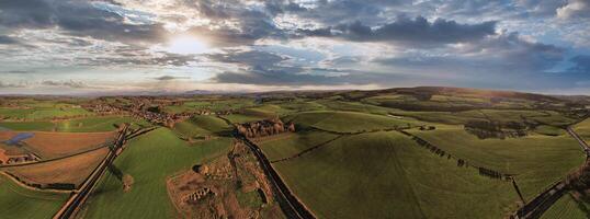 Panoramic aerial view of a scenic landscape with rolling hills, fields, and a winding road under a dramatic sky at sunset. photo