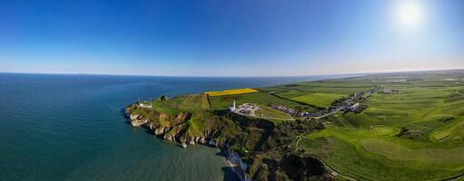 Panoramic view of a coastal landscape with cliffs, green fields, and a clear blue sky in Flamborough, England photo