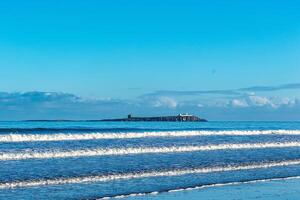 tranquilo marina con amable olas y distante isla debajo un claro azul cielo. foto