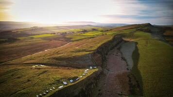 Aerial view of a scenic landscape with rolling hills, a meandering river, and a warm sunset glow at Sycamore Gap, Northumberland, UK. photo