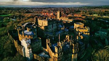 Aerial view of an ancient castle in Lancaster at sunset with lush greenery and a town in the background. photo