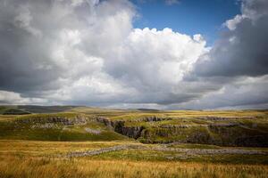 Dramatic landscape with expansive grasslands and rugged cliffs under a cloudy sky. photo