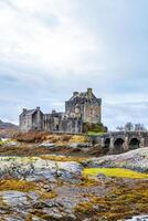 majestuoso medieval castillo con Roca puente terminado un río, rodeado por salvaje naturaleza debajo un nublado cielo en Escocia. foto