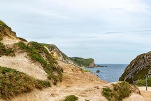 Coastal landscape with sandy cliffs and green vegetation under a cloudy sky, with a view of the ocean horizon. photo