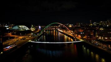 noche paisaje urbano con iluminado arco puente terminado río, reflejando luces en agua con urbano horizonte en Newcastle sobre Tyne foto