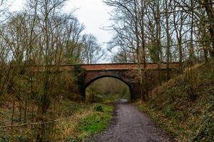 Rustic walking path leading to an old brick bridge surrounded by bare trees and greenery. photo