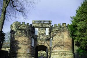 Medieval stone gatehouse with archway under a clear blue sky, surrounded by greenery. photo