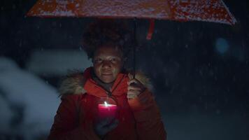 Young African Woman Standing on Street at Night During Snow Fall with Umbrella video