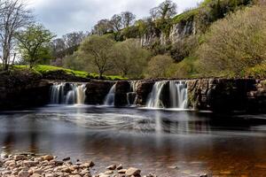 Tranquil waterfall in a lush green landscape with smooth water flow and rocky foreground in Yorkshire Dales. photo