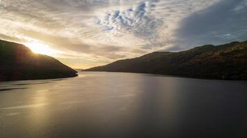 sereno lago a puesta de sol con Dom rayos perforación mediante nubes, rodeado por sierras. foto