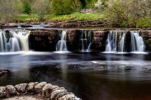 Serene waterfall cascading over rocks in a lush forest, captured with a slow shutter speed for a smooth water effect in Yorkshire Dales. photo