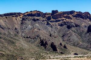 Scenic view of rugged mountains with a vast lava field in the foreground under a clear blue sky in the Teide, National Park, Tenerife photo