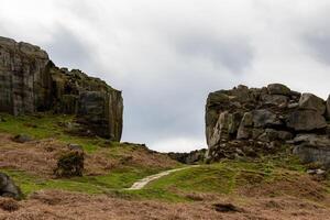 Rugged mountain path with rocky outcrops and green grass under a cloudy sky in Ilkley, Yorkshire photo